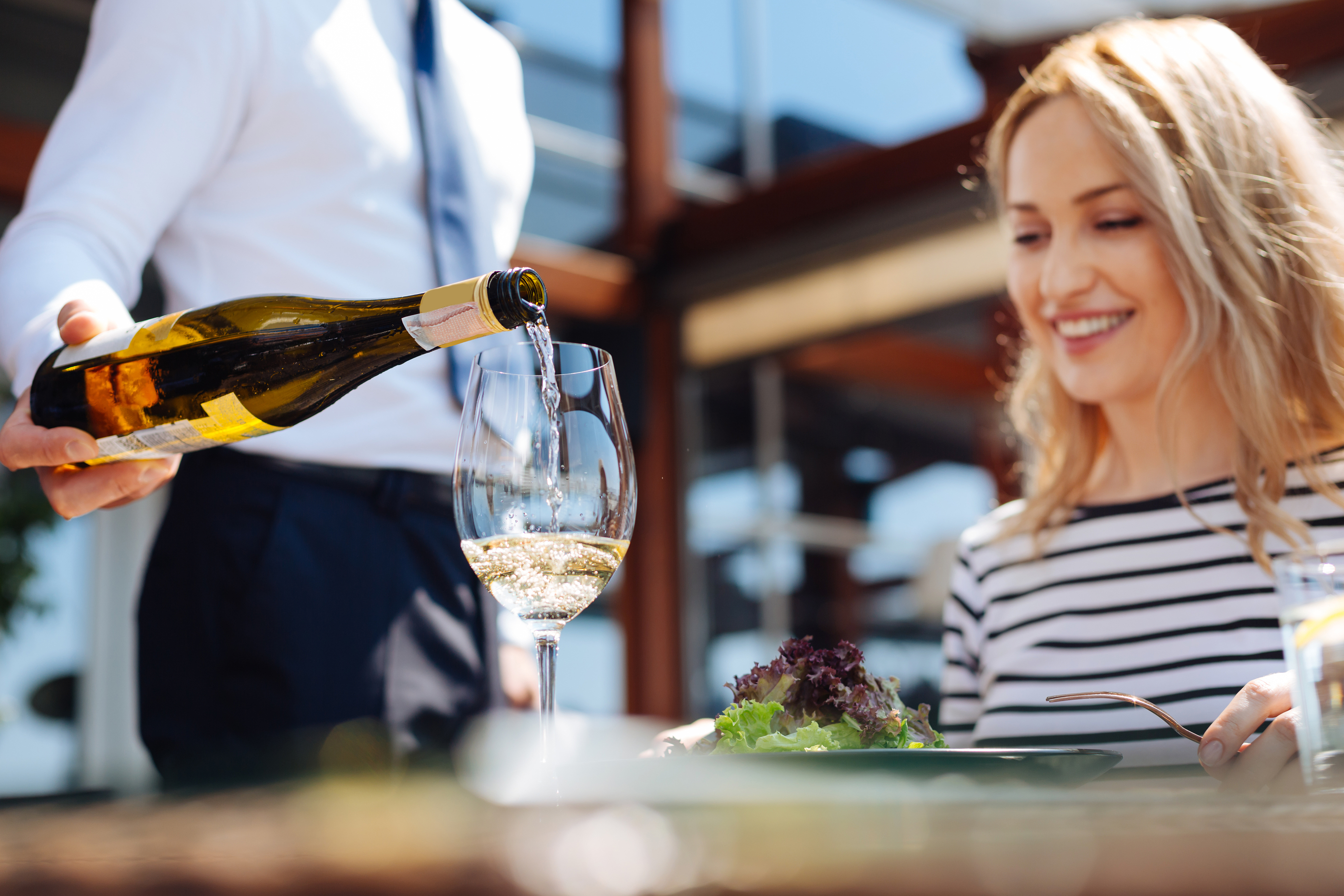 Server pouring wine for a happy customer at a restaurant